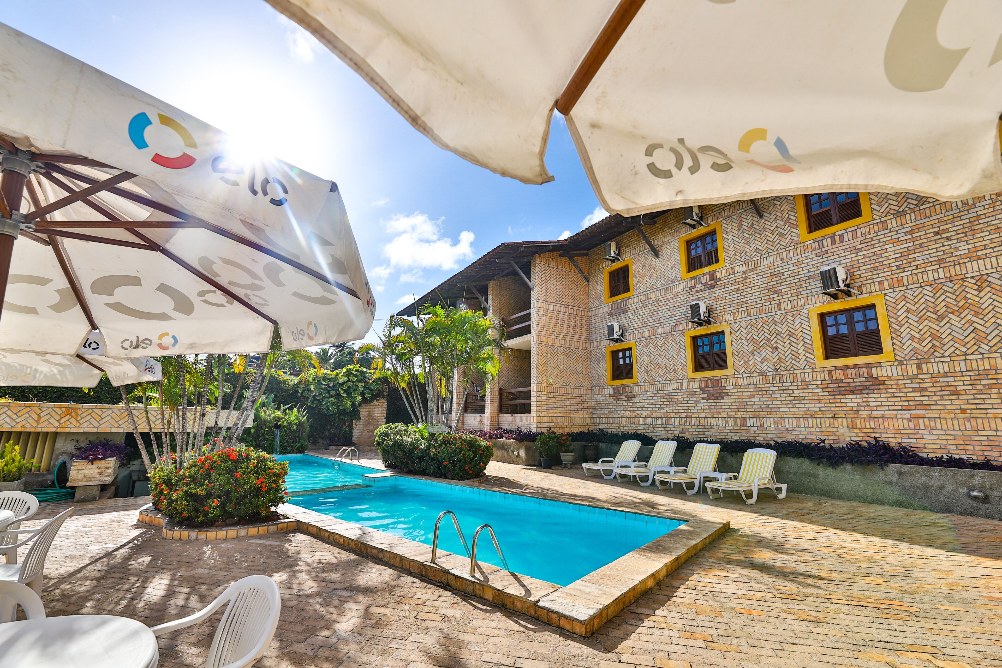 A pool area with a tiled pool, lounge chairs, umbrellas, and a brick building with patterned windows.
