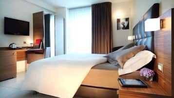 Una camera d'albergo moderna con un letto grande, una TV a schermo piatto, una scrivania con lampada e una finestra con tende.