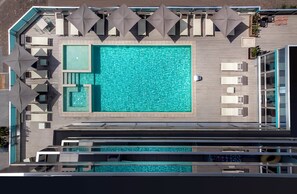 An aerial view of a swimming pool area with sun loungers and umbrellas, a separate hot tub, and a glass-enclosed section. - Aqua Hotel (Rimini)