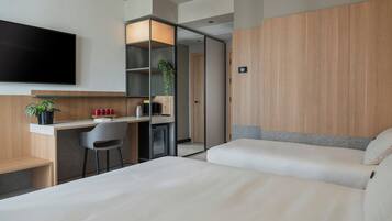 A modern hotel room with a desk, two beds, a TV, and a plant.