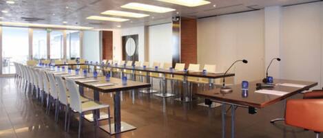 A conference room with long tables and chairs, equipped with microphones and nameplates.