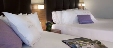 Una habitación de hotel con dos camas, cada una con ropa de cama blanca y varios cojines. Entre las camas hay una mesita de noche con un jarrón de flores.