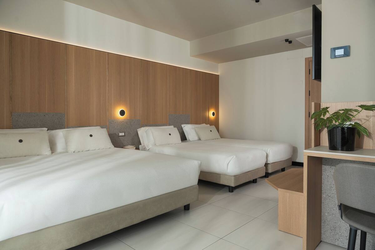 A hotel room with two beds, a desk, and a potted plant.