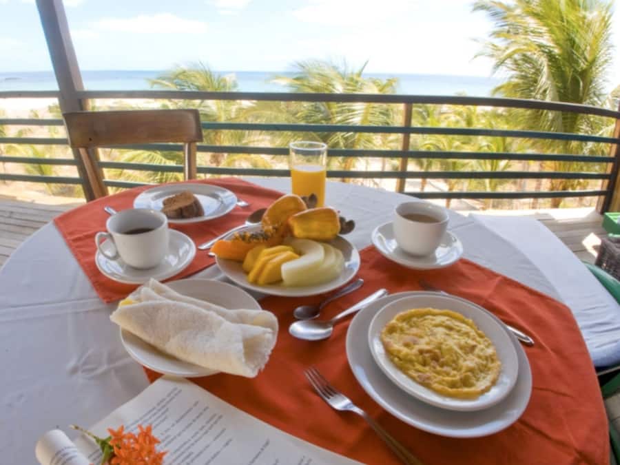 A table set with breakfast items, including eggs, toast, and juice, on a balcony with a view of the ocean.