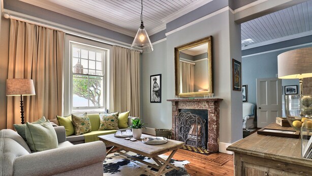 A cozy living room with a sofa, a coffee table, a fireplace, and a large mirror. - Parker Cottage (Cape Town)