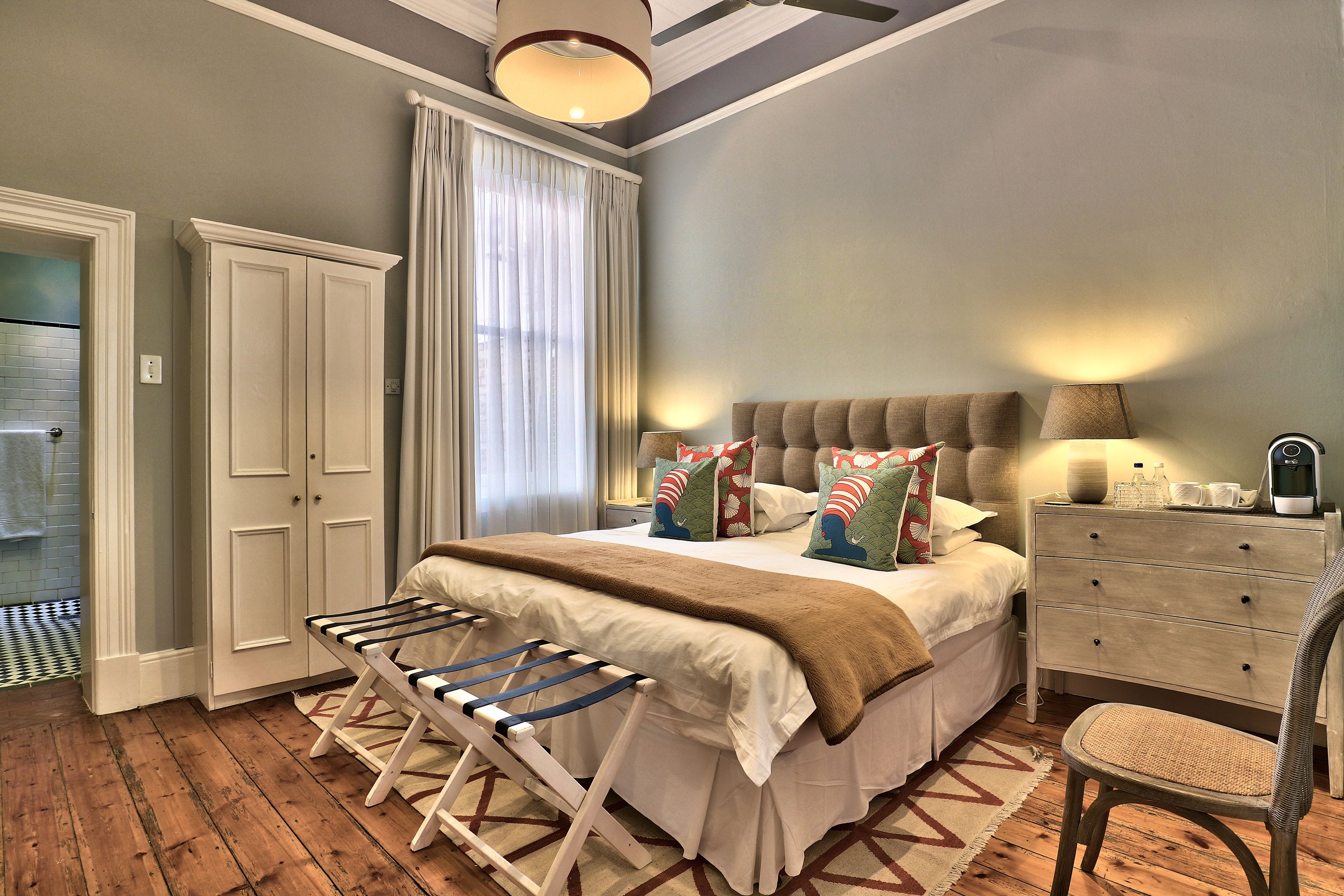 A bedroom with a bed, a dresser, a chair, a drying rack, and a window with curtains.