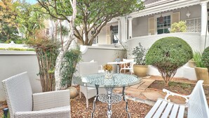 A patio with wicker furniture, a glass table, and a white bench. - Parker Cottage (Cape Town)