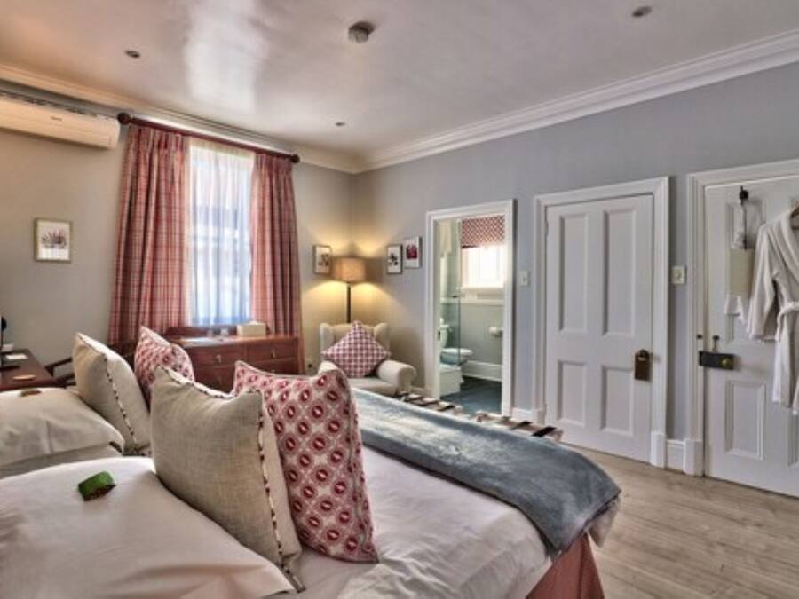 A hotel room with a bed, bedside tables, a lamp, a window with curtains, a mirror, and a door with a robe hanging on it.