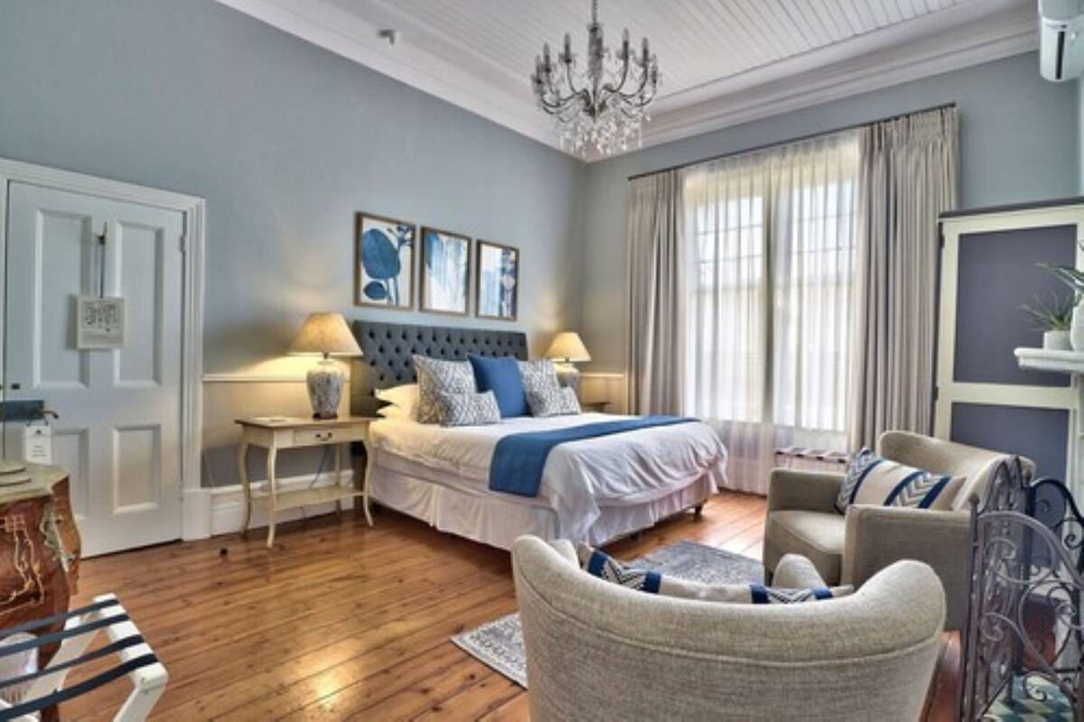 A bedroom with a bed, bedside tables, a chandelier, and a large window with curtains.