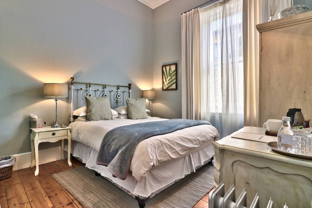 A neatly arranged bedroom with a bed, bedside tables, a dresser, and a window with curtains.