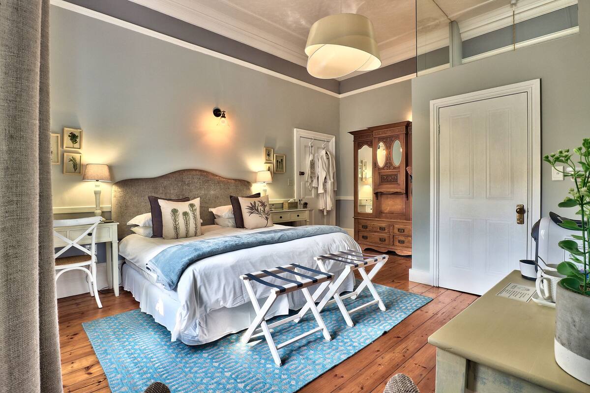 A bedroom with a bed, bedside tables, a dresser, a hanging rack, and a door.