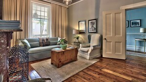 A living room with a sofa, armchair, coffee table, and a door leading to another room. - Parker Cottage (Cape Town)