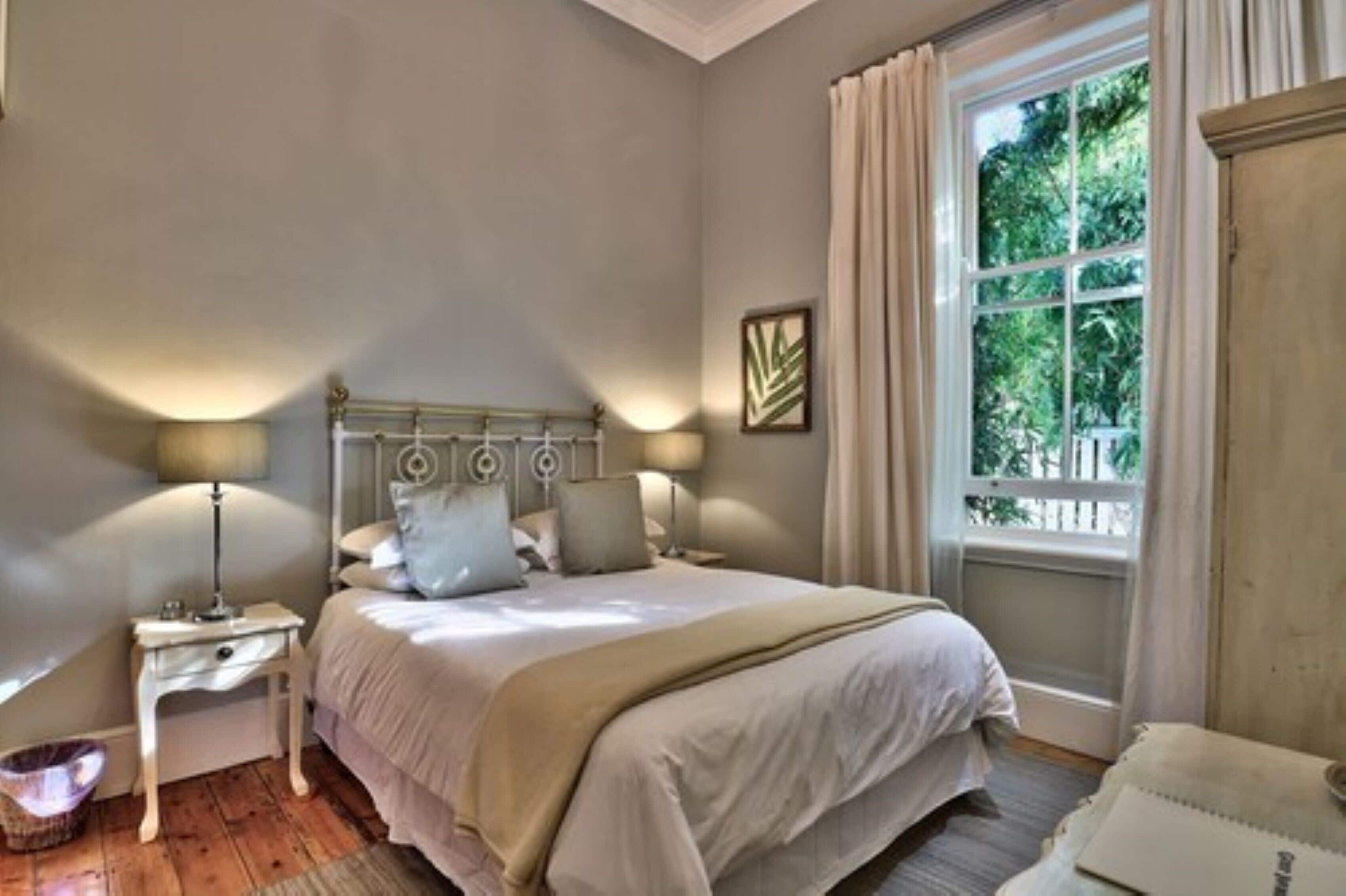 A bedroom with a bed, bedside tables, a window with curtains, and a view of greenery outside.