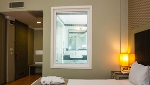 A hotel room with a bed, two towels, a nightstand with a lamp, and a view of the bathroom through a window. - Hotellino (Istanbul)