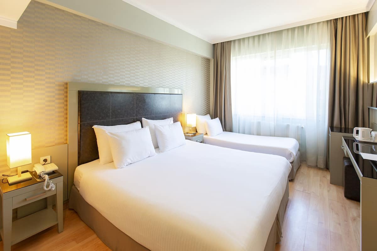 A hotel room with two beds, a desk, a telephone, and a window with curtains.