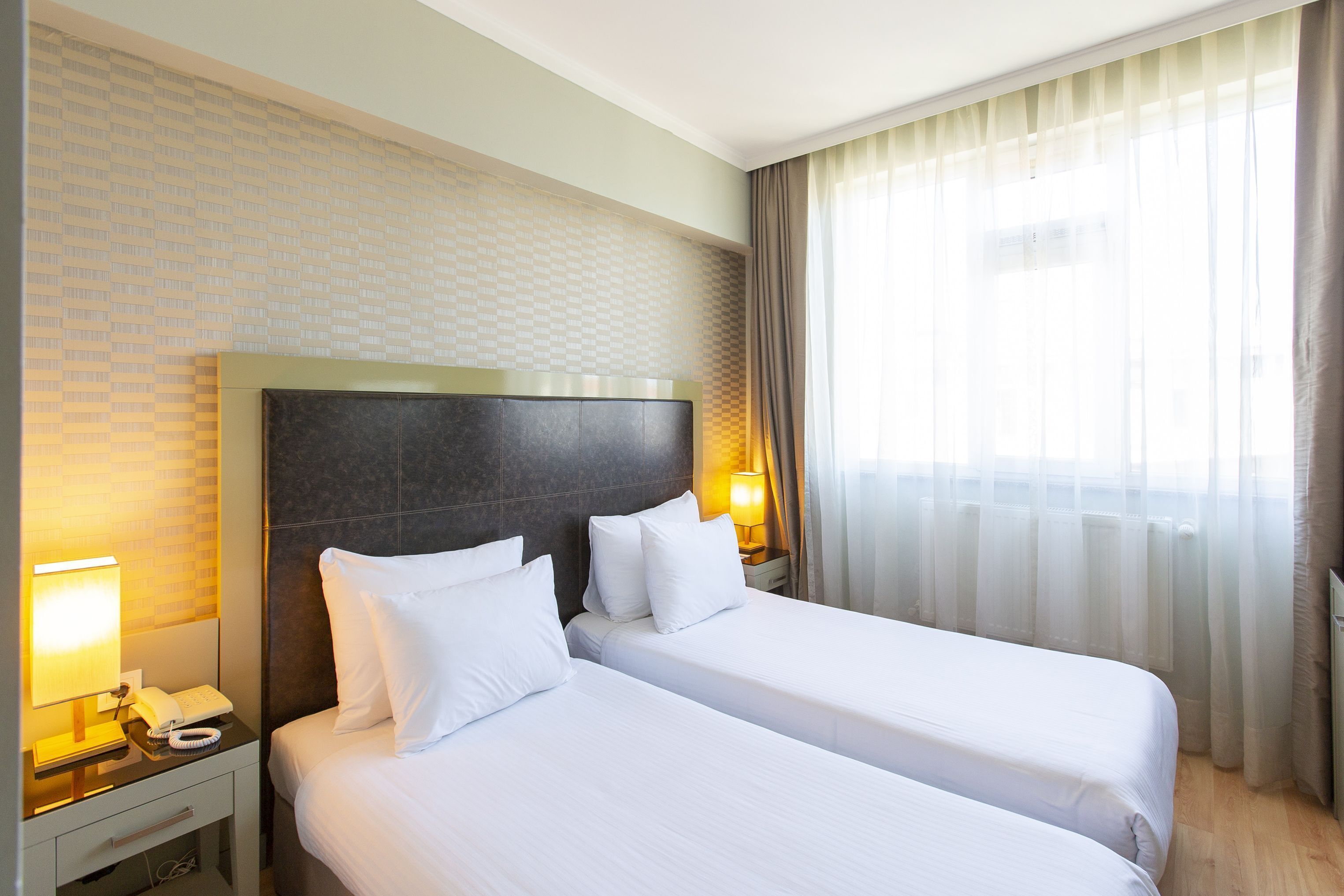 Ein Hotelzimmer mit zwei Betten, einem Nachttisch mit Lampe und einem Fenster mit Vorhängen.