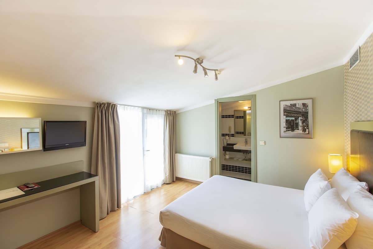 A hotel room with a bed, a desk, a television, a bathroom, and a view of the outside.