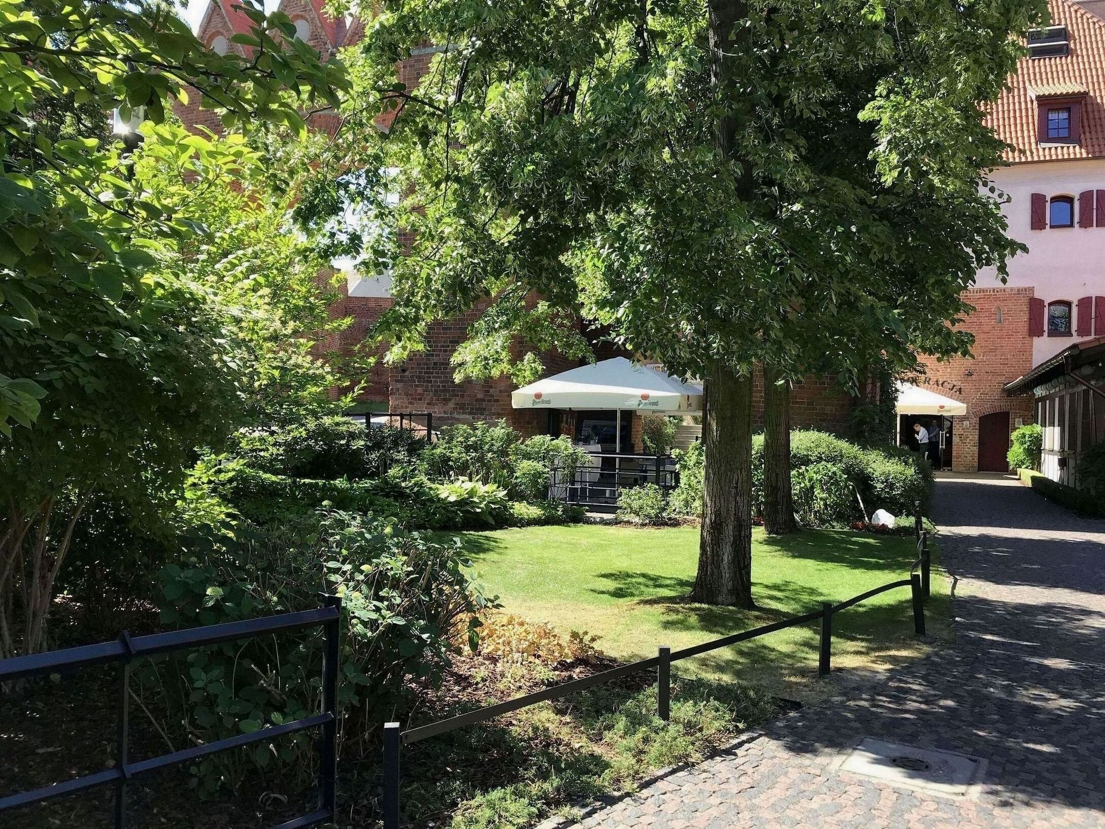 A courtyard with a brick building, a covered seating area, and a tree providing shade.