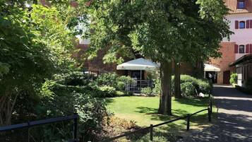 A courtyard with a brick building, a covered seating area, and a tree providing shade.