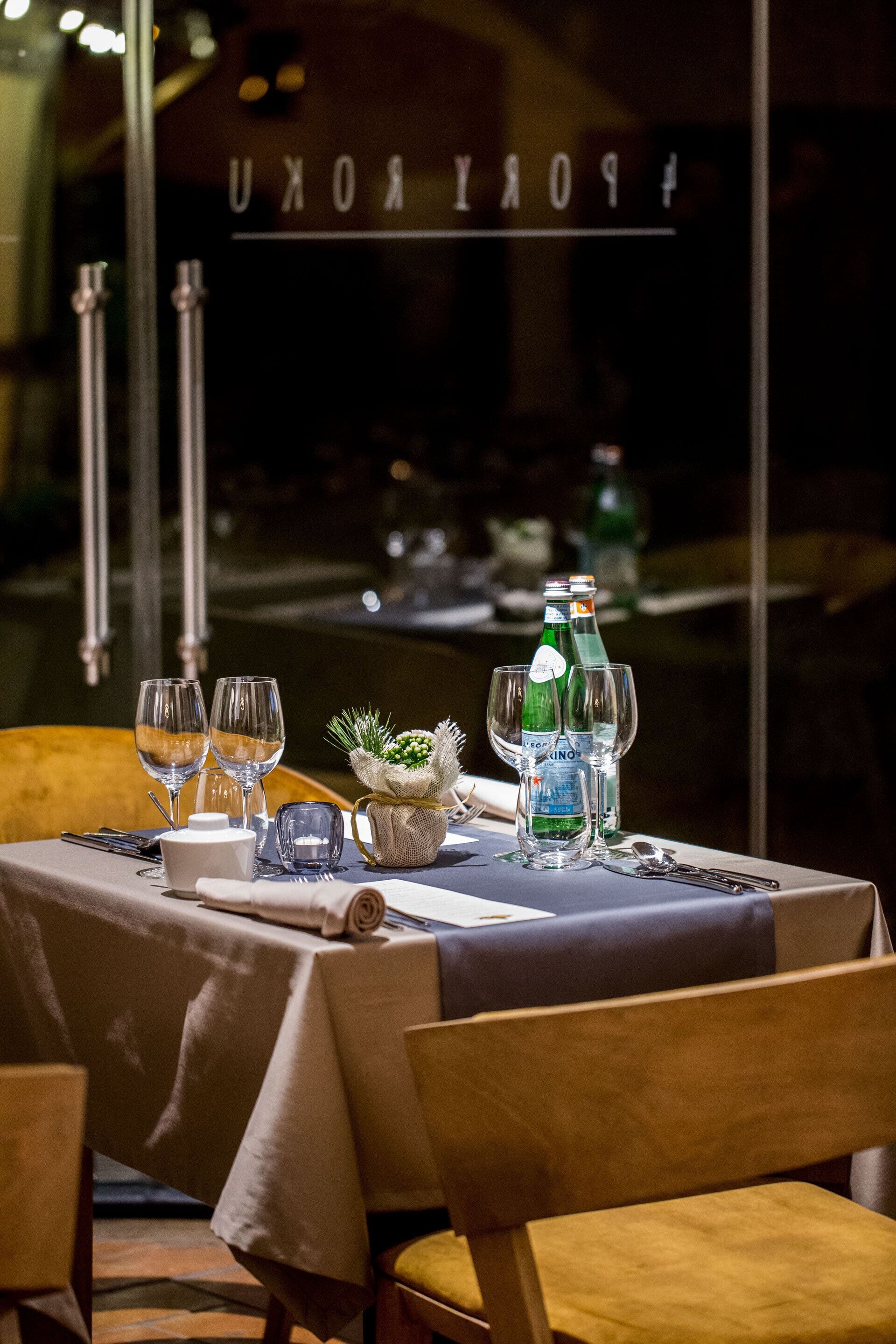 A dining table set with wine glasses, bottles, and a small decorative plant.