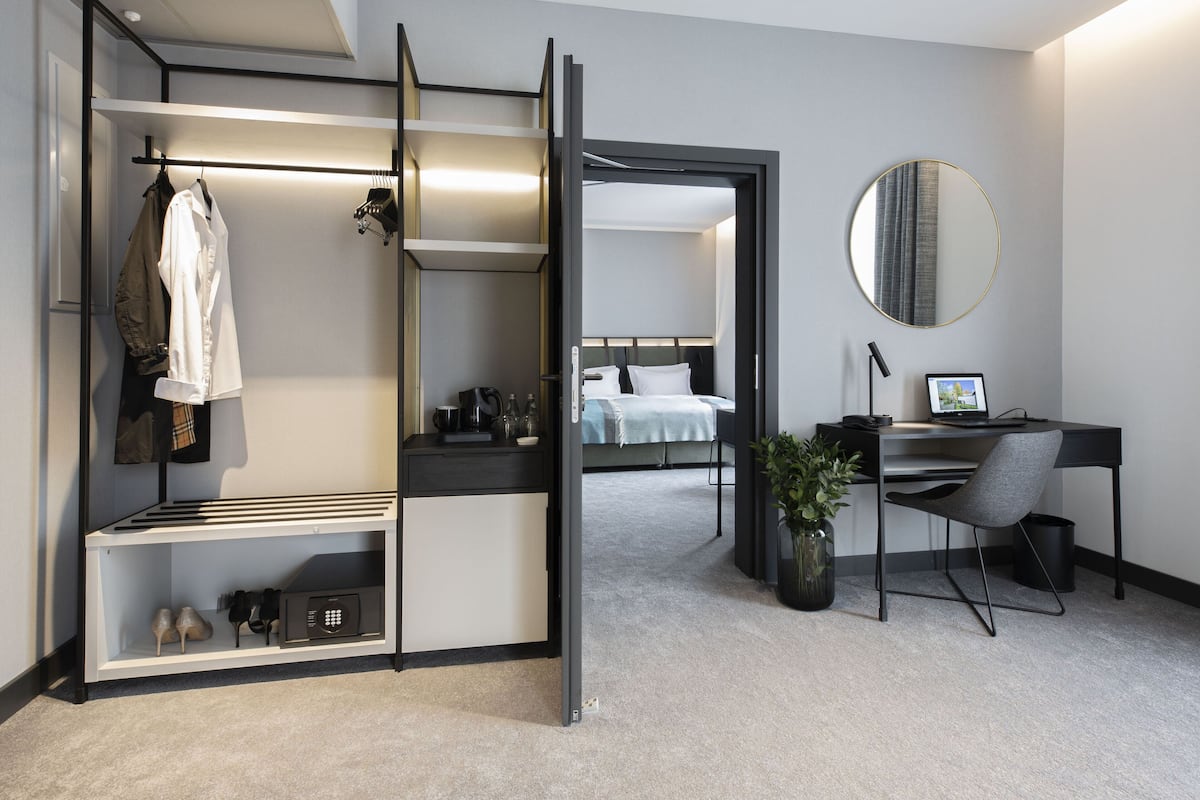 A modern hotel room with a split bed, a desk with a laptop, a mirror, and a shoe rack.