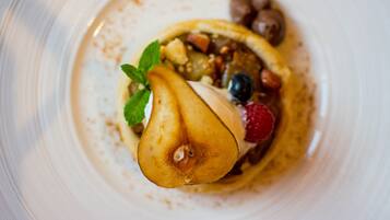 Un dessert con una pera, mirtilli, lamponi e un ciuffo di menta su un piatto bianco.