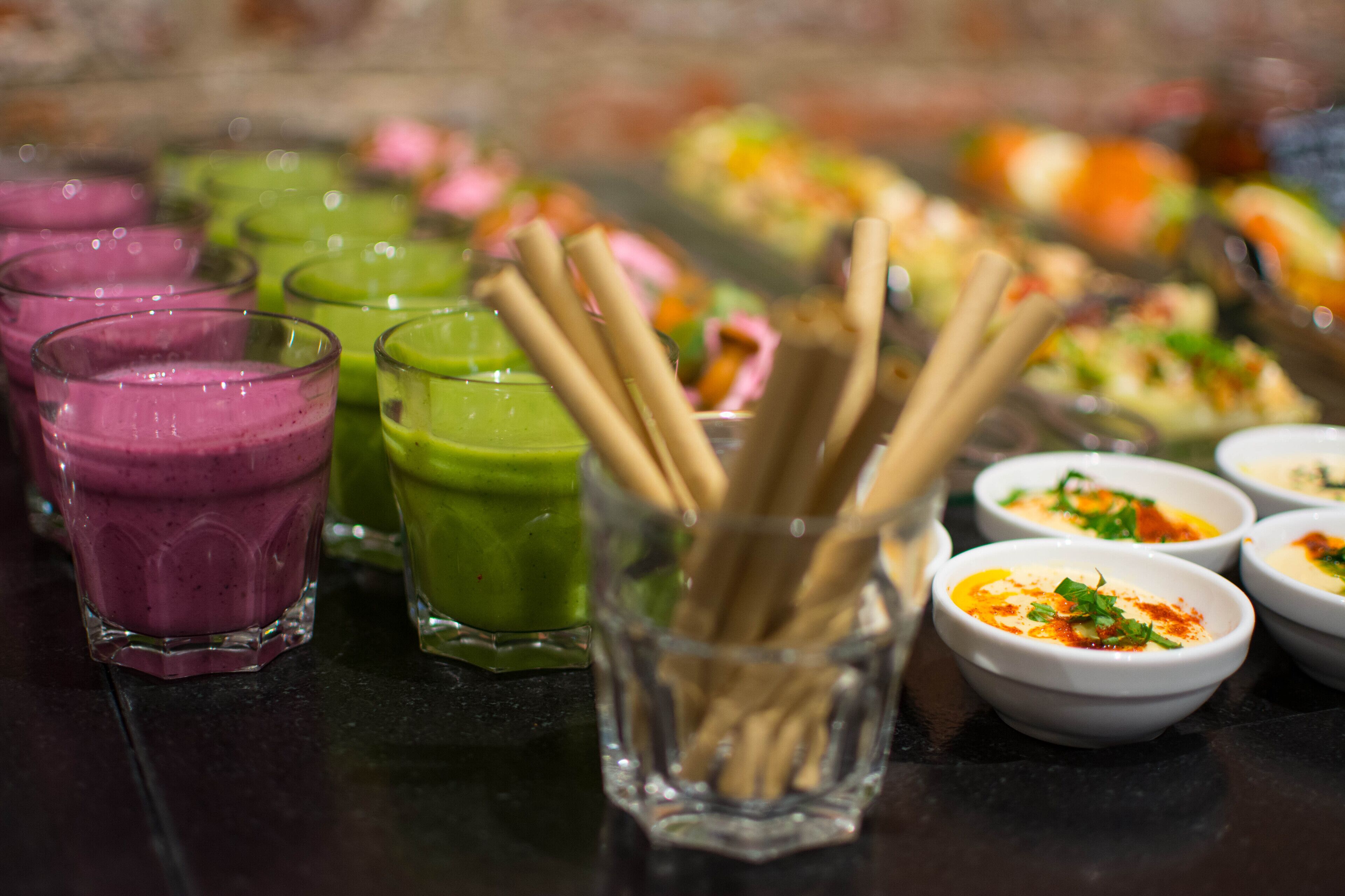 Variedad de bebidas coloridas y pequeños recipientes con comida sobre una mesa.