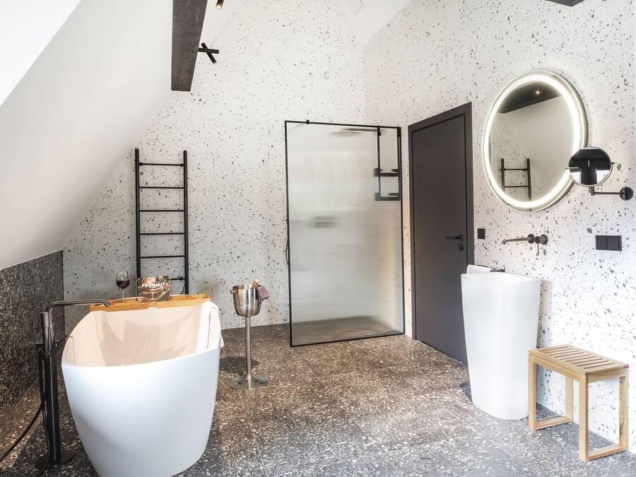 A modern bathroom with a freestanding bathtub, a shower enclosure, a round mirror, and a small wooden stool.