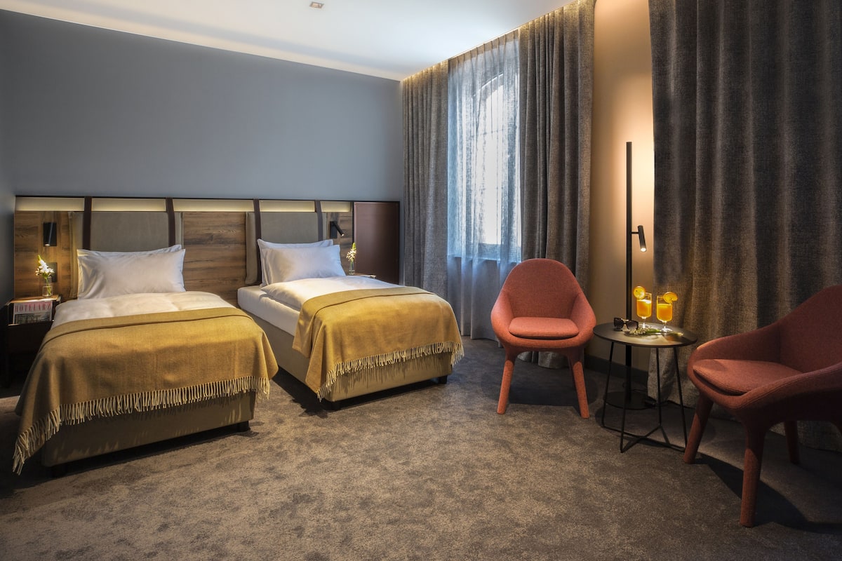 A hotel room with two beds, a sitting area with two chairs, a small table with drinks, and a large window with curtains.