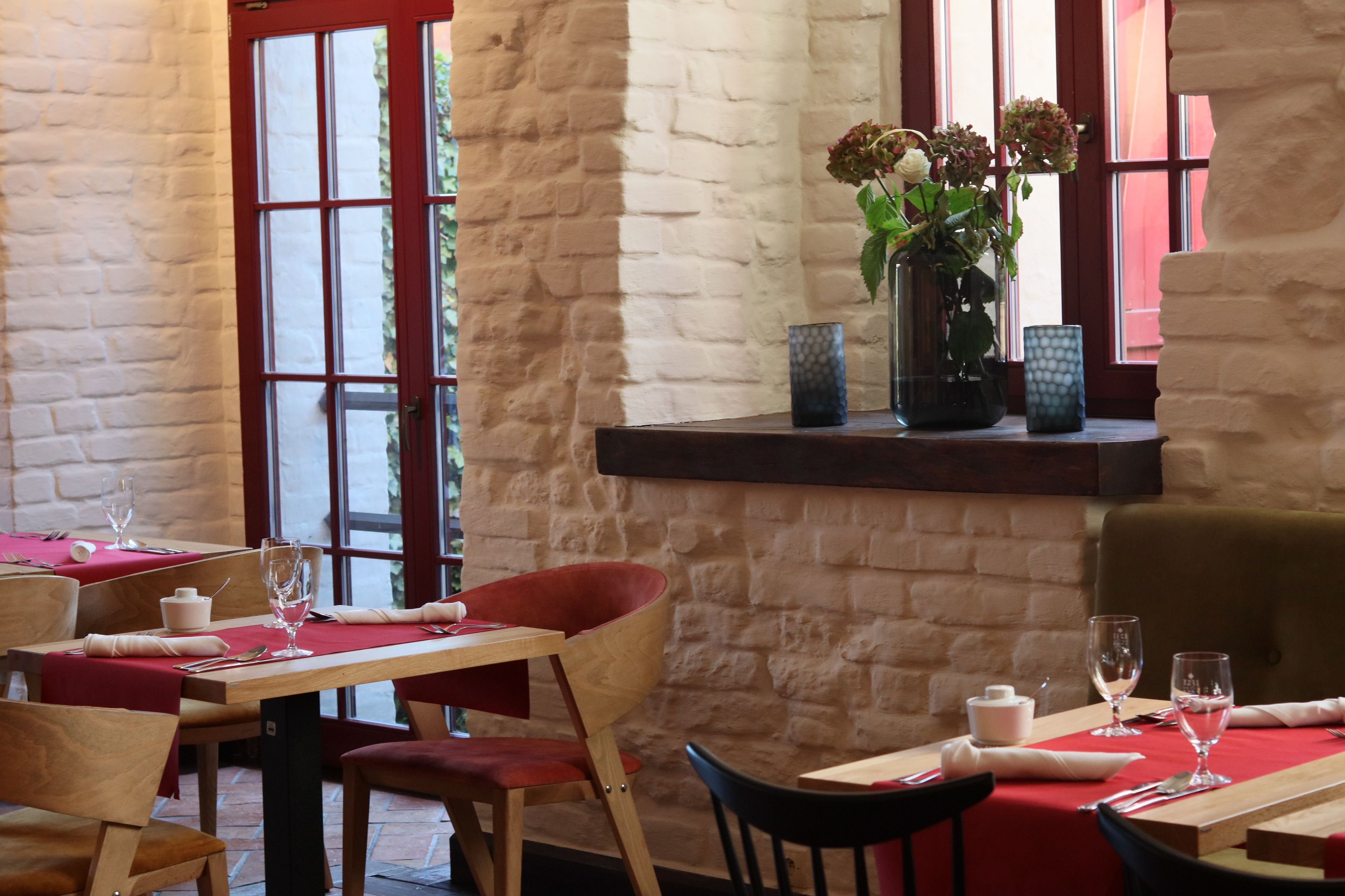 En restaurantindretning med stenvægge, træborde og røde stole.
