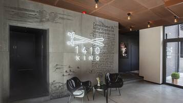 A modern interior with a concrete wall featuring a neon sign and a large number '1410'. There are two black chairs and a small table with a vase.