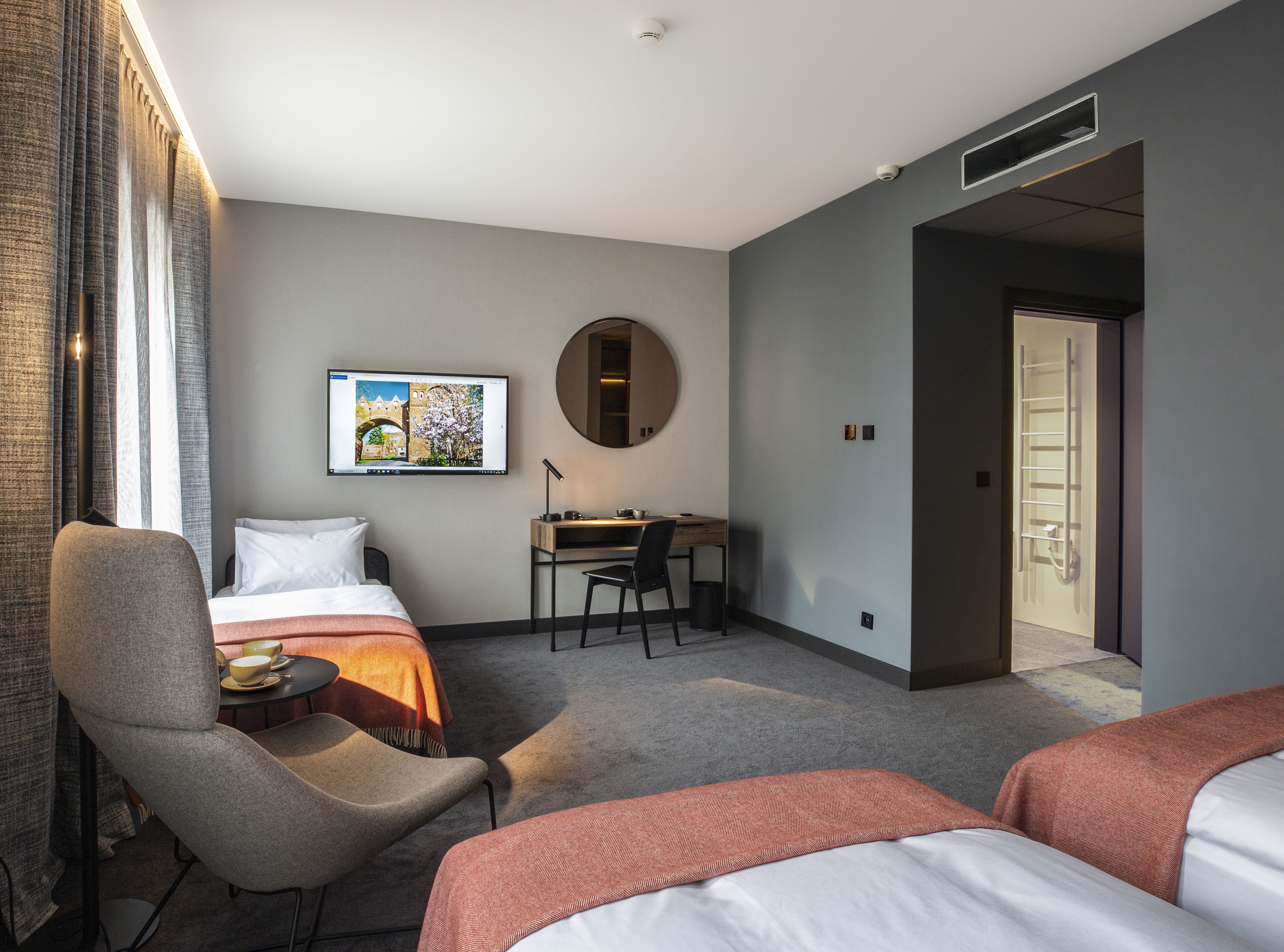 Une chambre d’hôtel équipée d’un lit, d’un bureau, d’une chaise et d’un téléviseur diffusant une image de paysage.