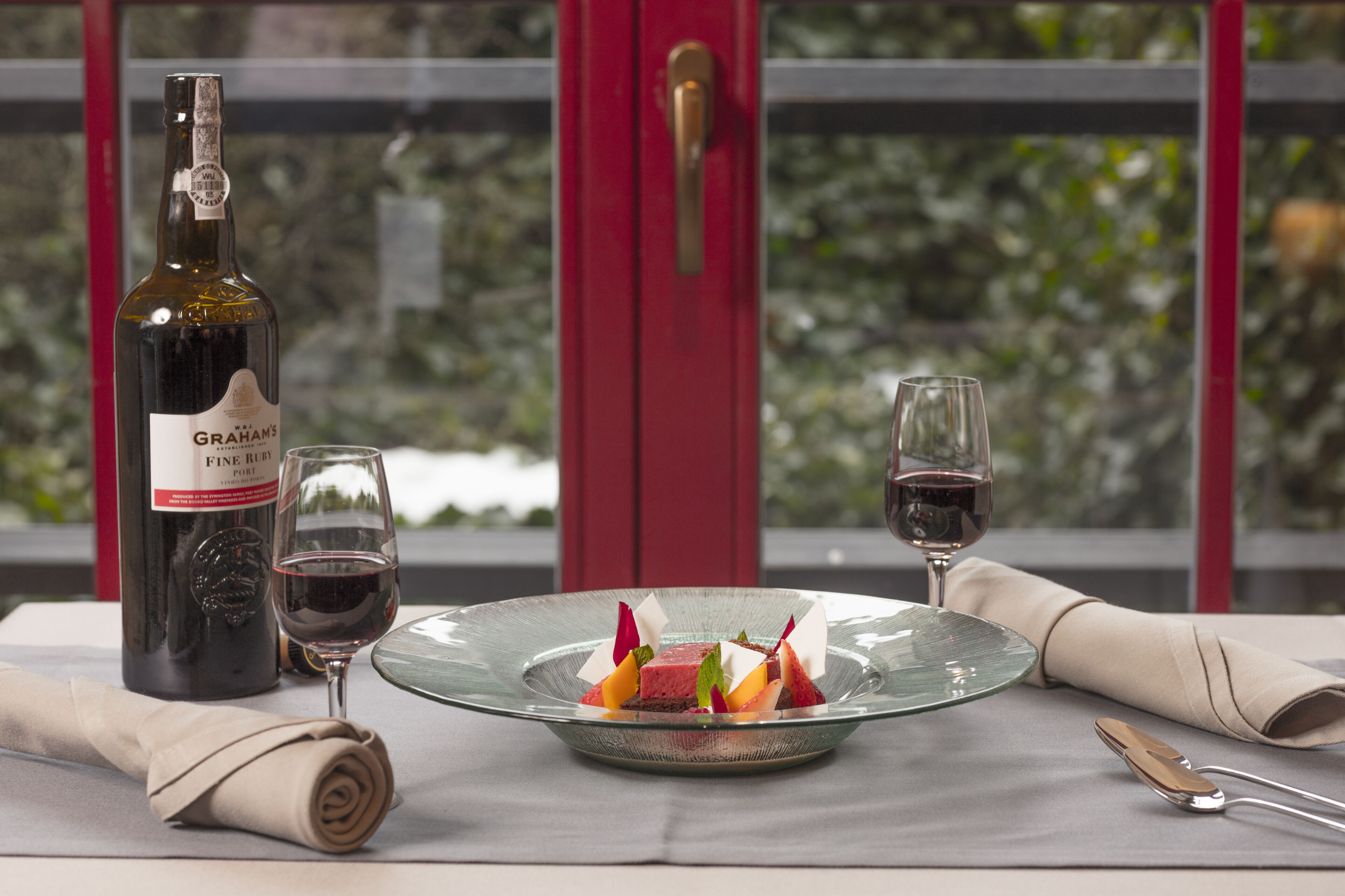 Una mesa con una botella de vino, dos copas, un servilleta doblada y un plato de postre.