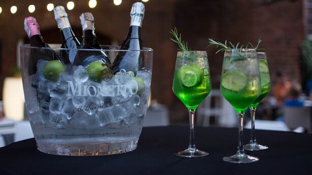Recipiente de vidro com garrafas e dois copos com bebidas verdes e gelo.