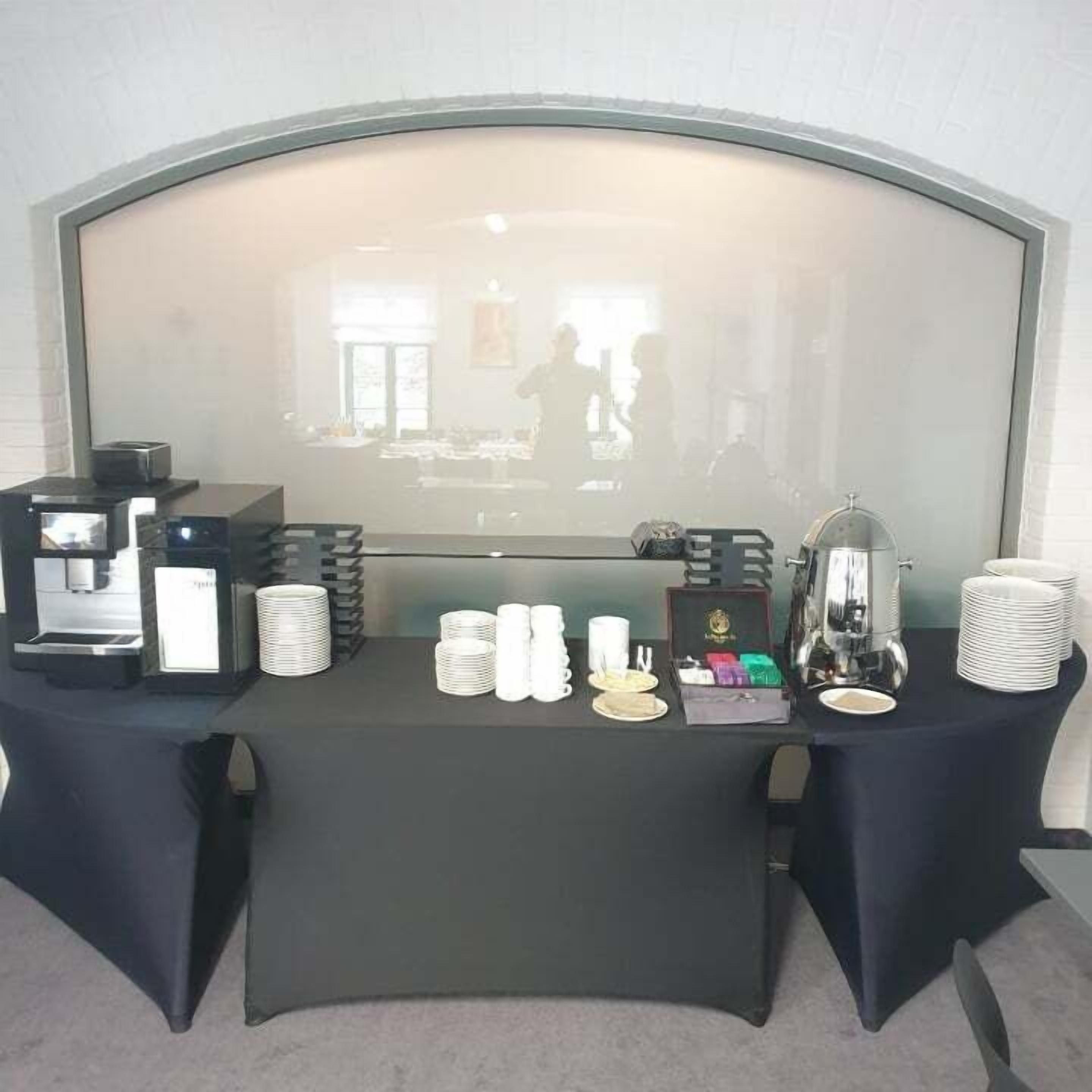 A breakfast bar with coffee machines, white cups, and a glass display case.