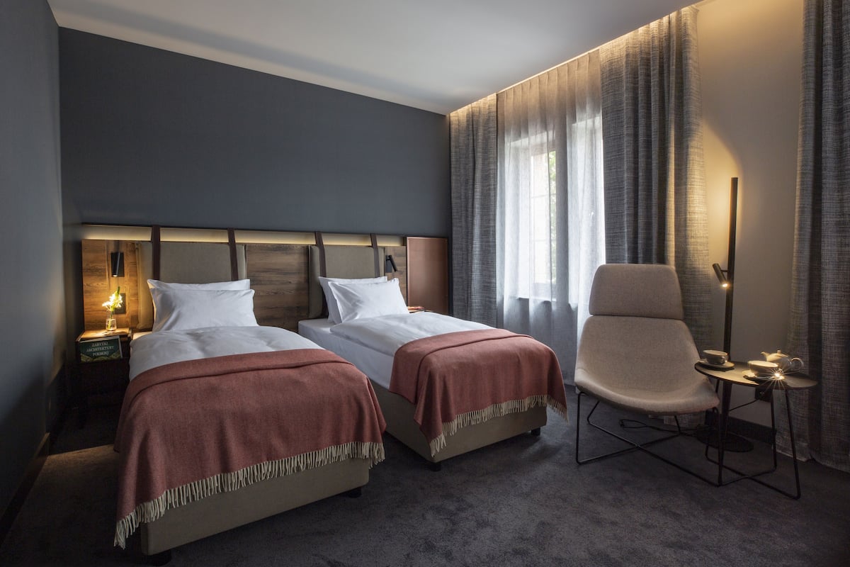 A hotel room with two beds, a chair, a nightstand, and a lamp.