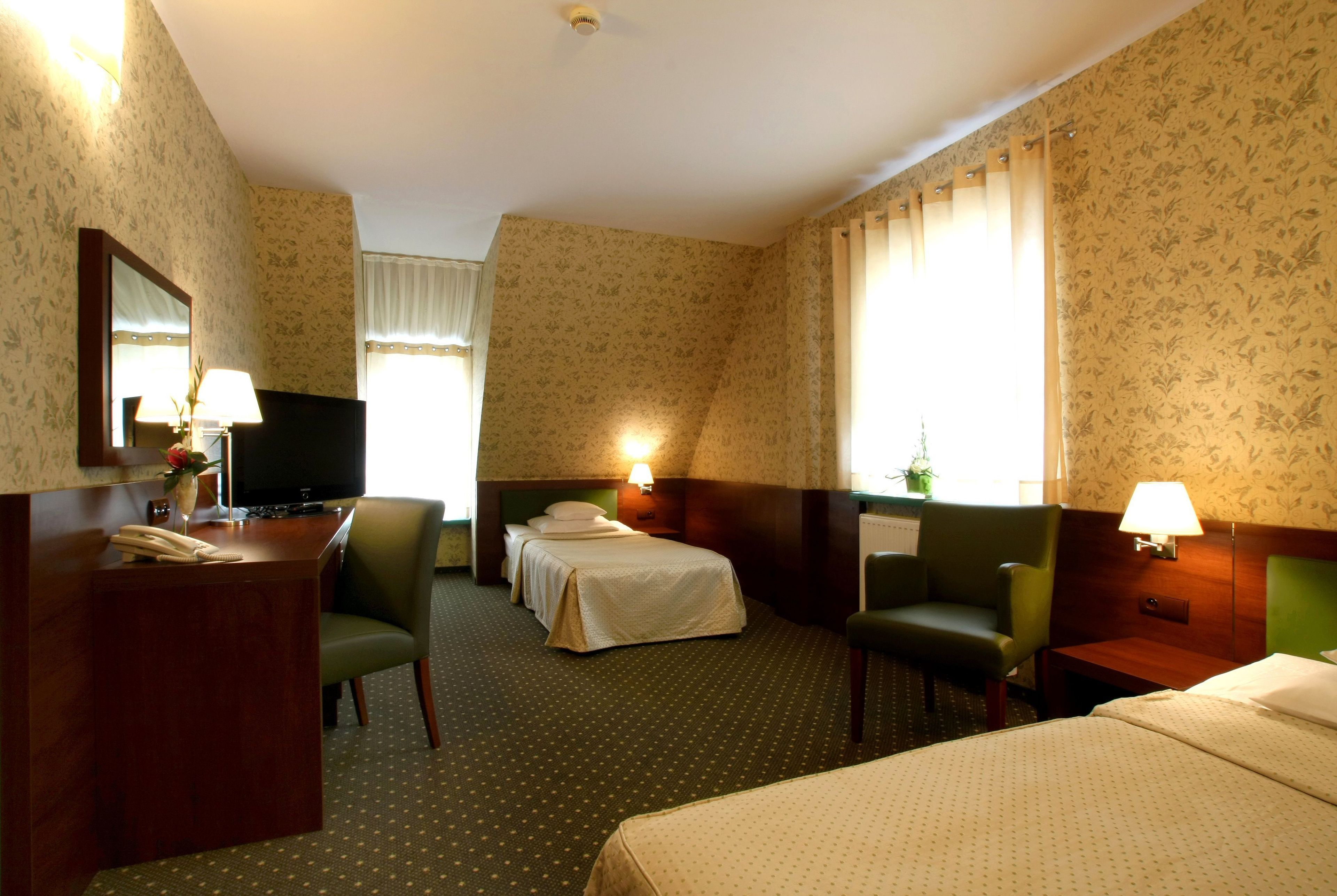 Habitación de hotel con cama, dos sillas, escritorio con teléfono, televisión y dos lámparas de noche.