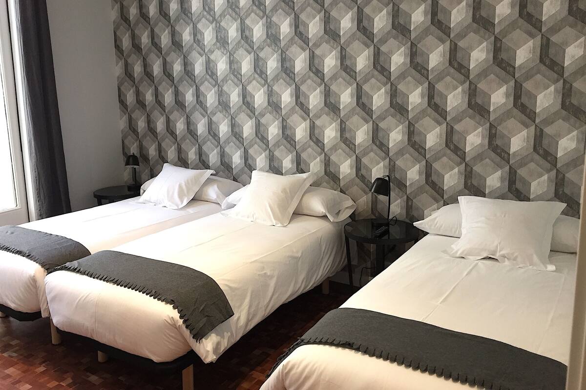 A hotel room with two beds, a geometric patterned wall, and a small bedside table with a lamp.