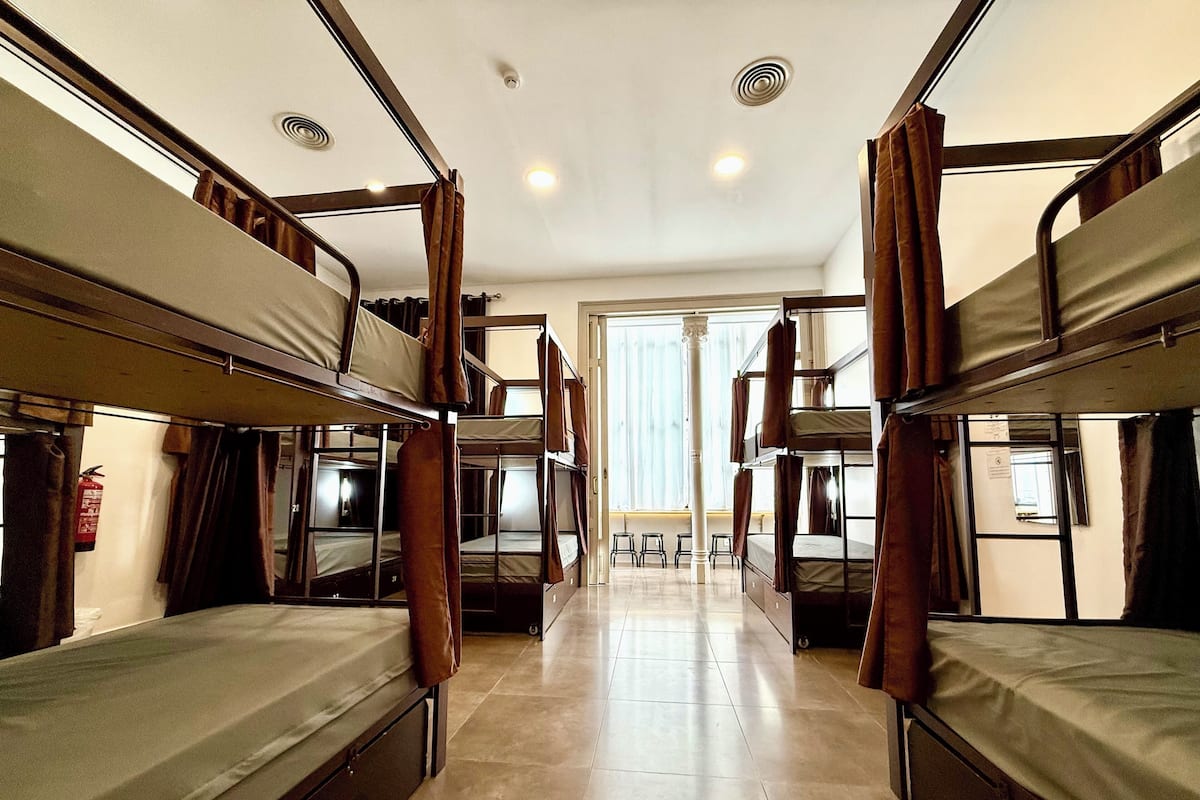 A dormitory room with bunk beds, a fire extinguisher, and a view of the outside through a large window.