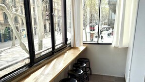 A room with a long window, a wooden ledge with black stools, and a tiled floor. - Hip Karma Hostel (Barcelona)