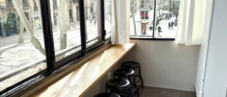 Una habitación con un ventanal largo, un repisa de madera con taburetes negros y suelo de baldosas.