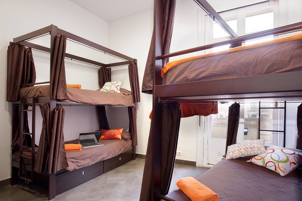 A bunk bed room with a laptop on the lower bunk, a ladder, and a window with curtains.