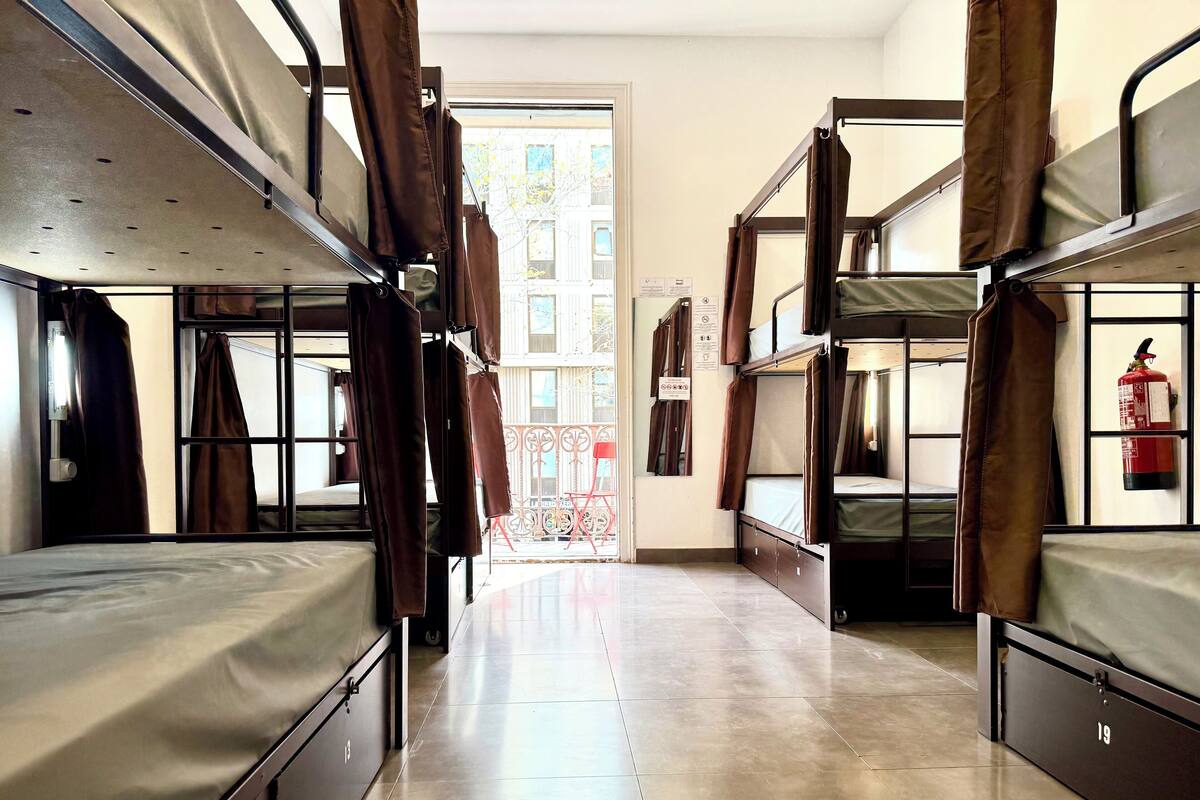 A dormitory room with bunk beds, a fire extinguisher, and a view of the outside.