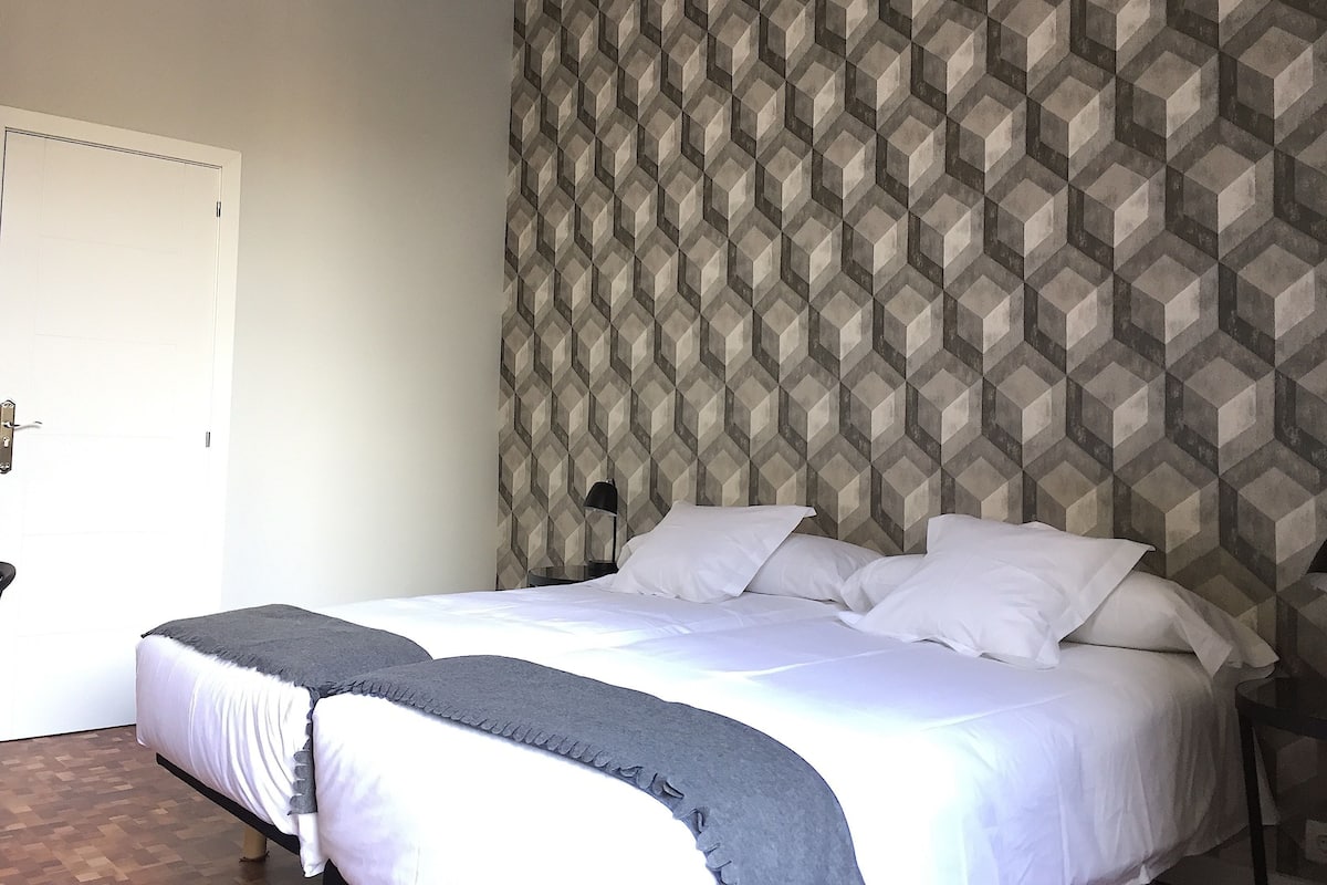 A hotel room with a bed, a door, and a patterned wall.
