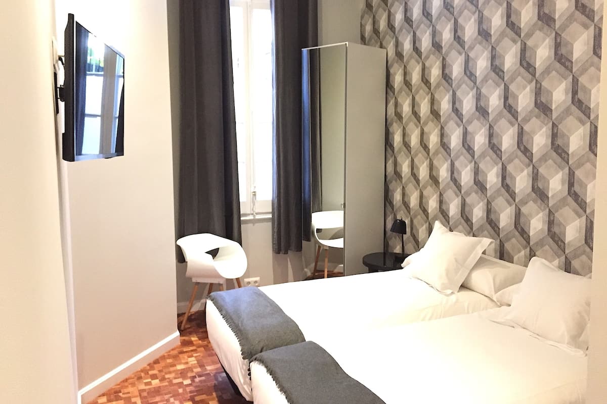 A hotel room with a bed, a chair, a mirror, and a patterned wall.