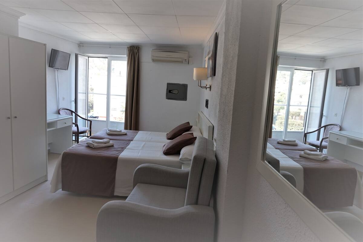 A hotel room with a large bed, two bedside tables, a TV, and a window with curtains.