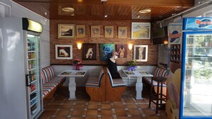 A restaurant with wooden ceiling, brick walls, and artwork. There are booths, tables, and a vending machine. - Hermes (Tossa de Mar)