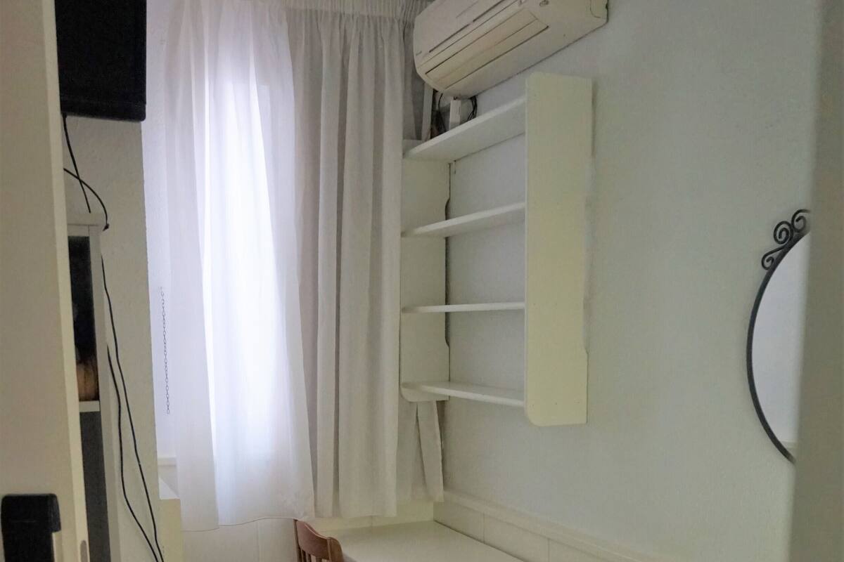 A small, clean room with a bed, a desk, and a shelf unit.