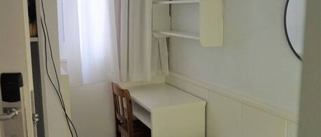 A small, clean room with a bed, a desk, and a shelf unit.