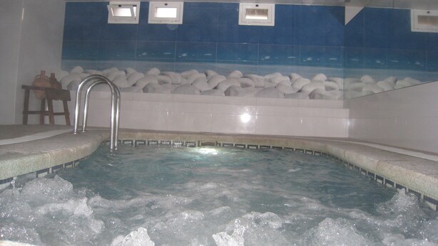 A hot tub with a stone wall backdrop, a wooden stool, and a tiled ceiling. - Hermes (Tossa de Mar)